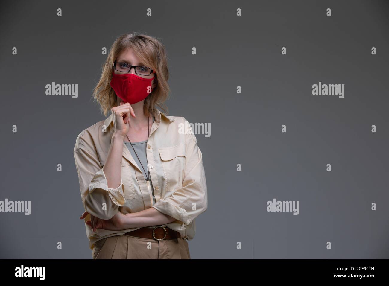 Rubia joven en máscara protectora roja contra los virus, sostiene su cabeza. Foto de stock