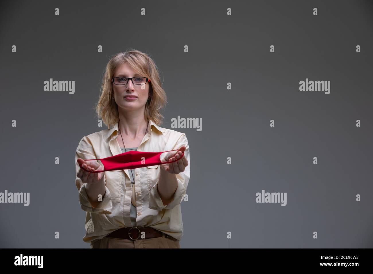 Rubia joven en máscara protectora roja contra los virus, sostiene su cabeza. Foto de stock