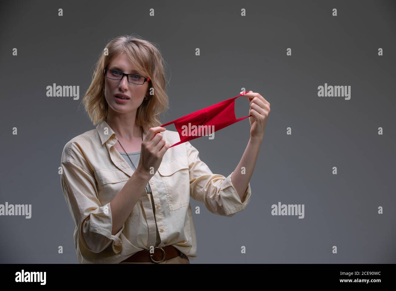 Rubia joven en máscara protectora roja contra los virus, sostiene su cabeza. Foto de stock