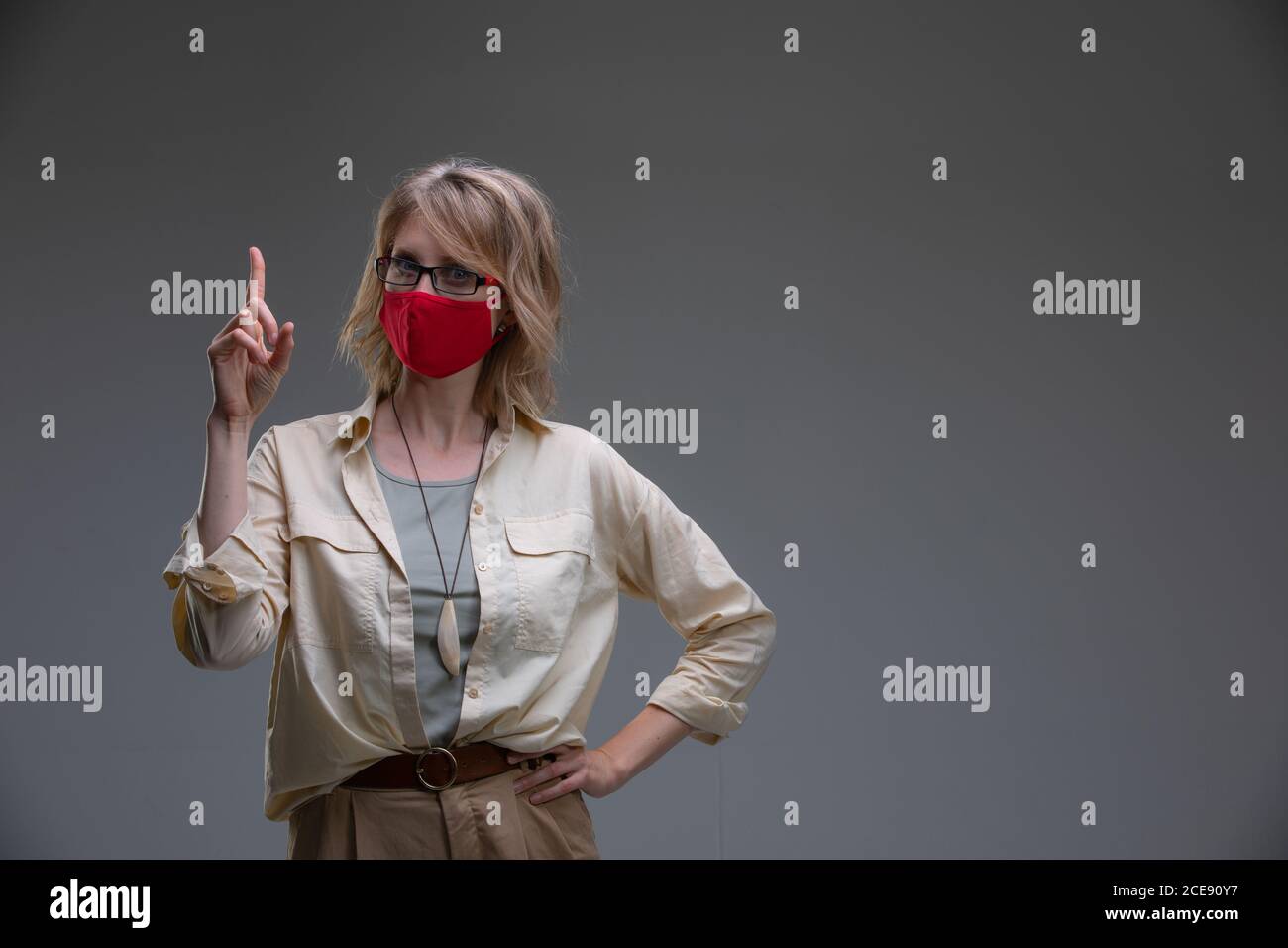 Rubia joven en máscara protectora roja contra los virus, sostiene su cabeza. Foto de stock