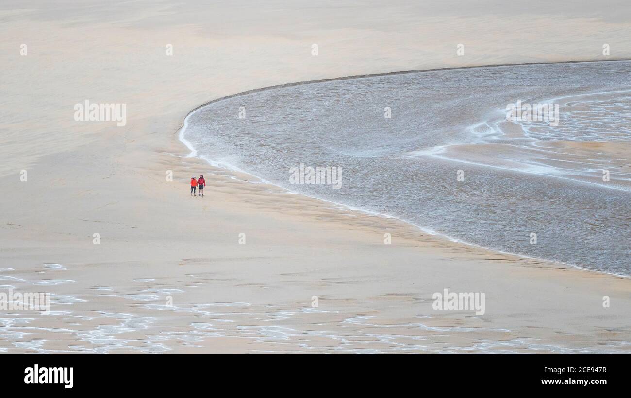 Una imagen panorámica de los senderistas vistos desde una distancia caminando en marea baja a través de Crantock Beach mientras el río Gannel fluye al mar en Newquay en Cornwall. Foto de stock