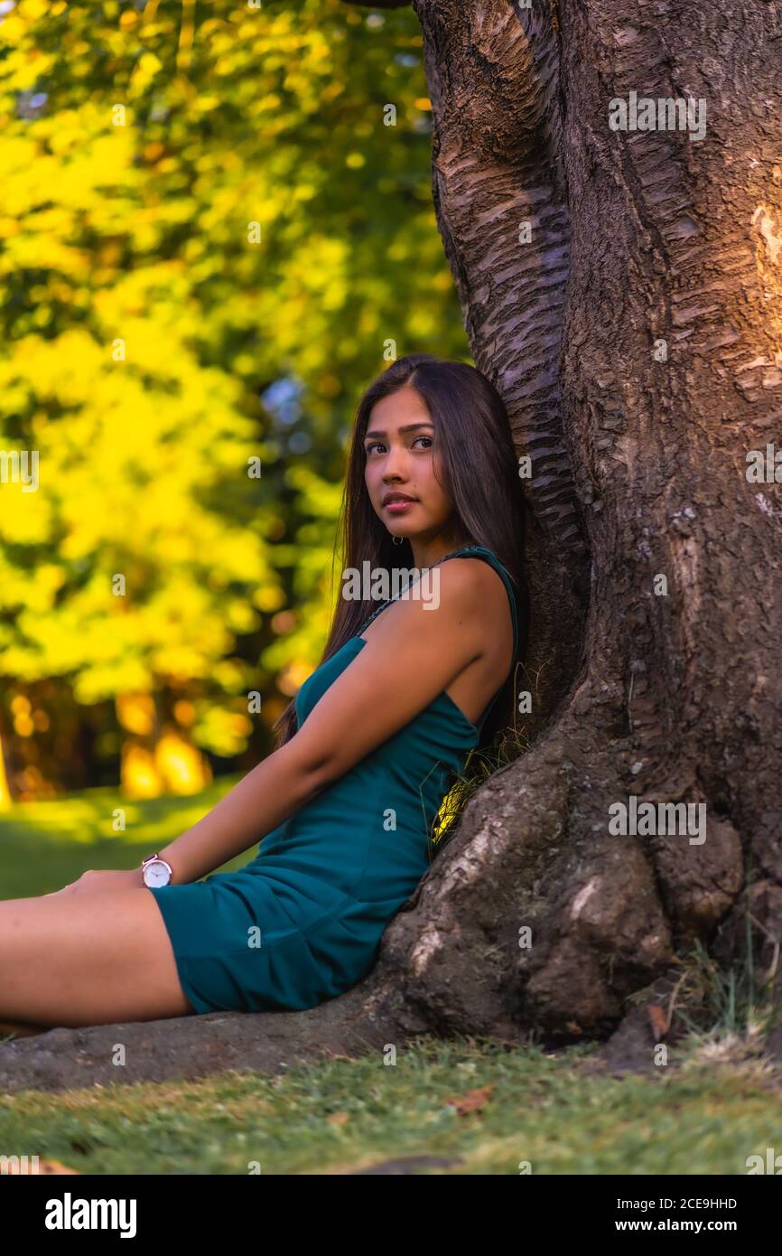 Joven morena latina con pelo largo y recto apoyado contra un árbol en un vestido  verde Fotografía de stock - Alamy