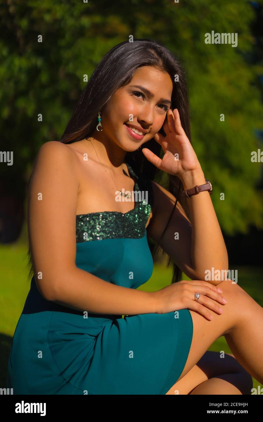 Joven morena latina con pelo largo y recto apoyado contra un árbol en un vestido  verde Fotografía de stock - Alamy