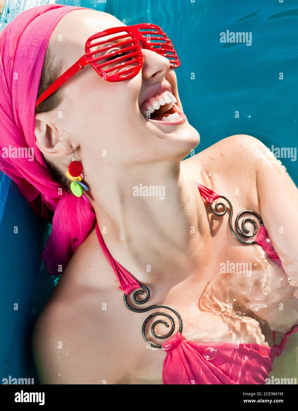 mujer sonriente con gafas de sol rojas en la piscina Foto de stock