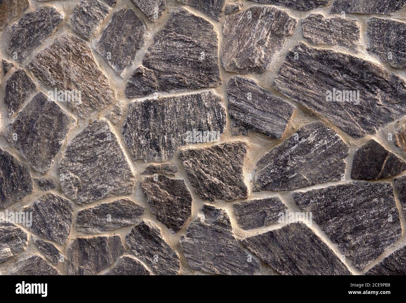 Piedras de granito gris natural incrustadas en la pared de estuco una casa que forma un patrón de mosaico Foto de stock