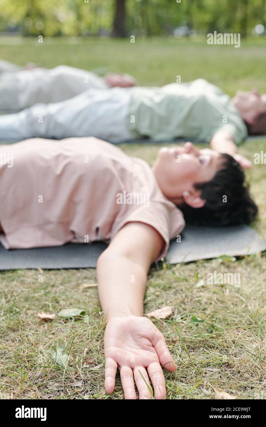Primer plano de mujer tranquila acostada con los brazos estirados sobre la hierba y relajarse en shavasana después de la práctica de yoga Foto de stock