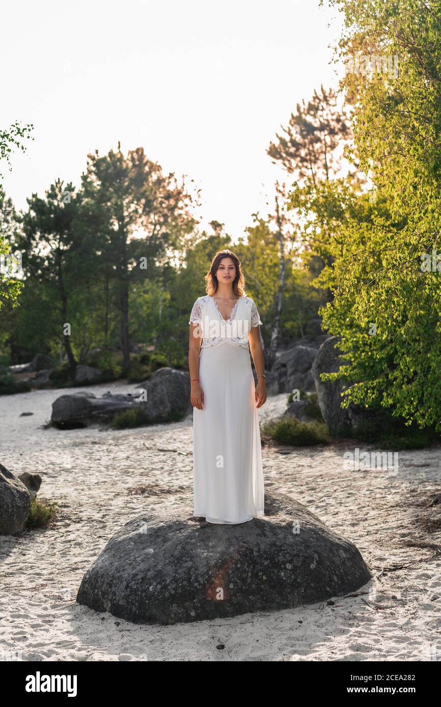 Mujer adulta con elegante encaje vestido blanco de novia y de pie en la  roca en la costa arenosa en verde follaje de aspecto en la cámara  Fotografía de stock - Alamy