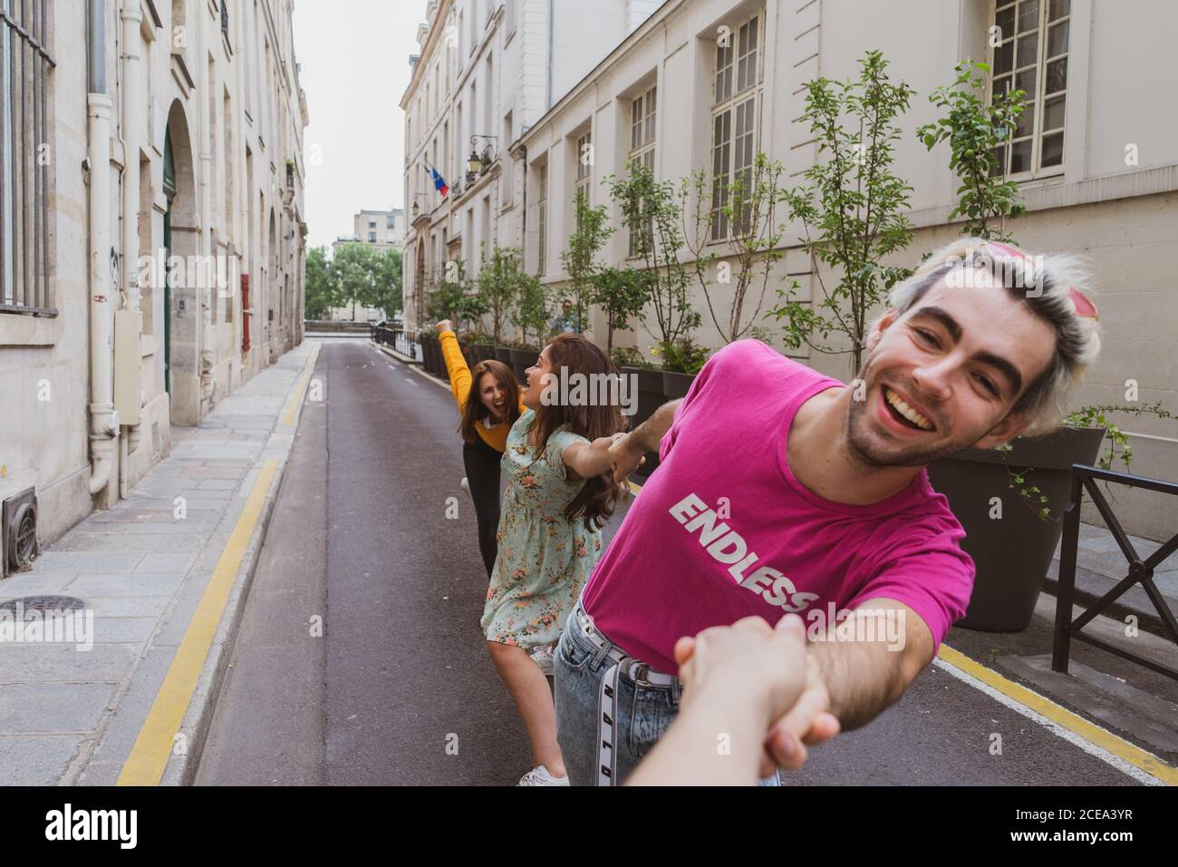 Reírse de mujeres bonitas con ropa informal y de moda barbudo hombre Tirando de las manos de pie a lo largo de la estrecha calle europea Foto de stock