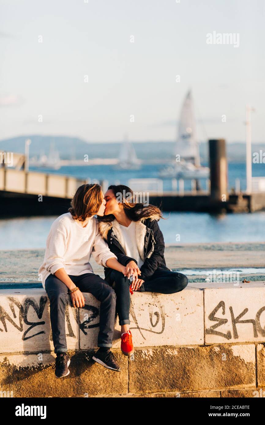 Beso entre el hombre y la mujer en ropa casual sentado en terraplén cerca  del agua sobre fondo borroso Fotografía de stock - Alamy