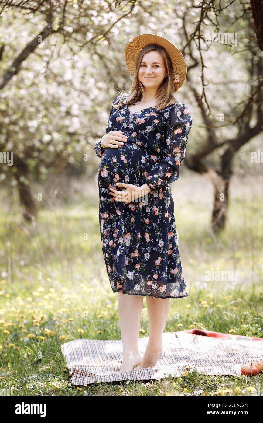 Una hermosa mujer embarazada en un sombrero de paja en el parque de flores  de primavera. La madre embarazada camina en el jardín de primavera.  Esperando un milagro Fotografía de stock -