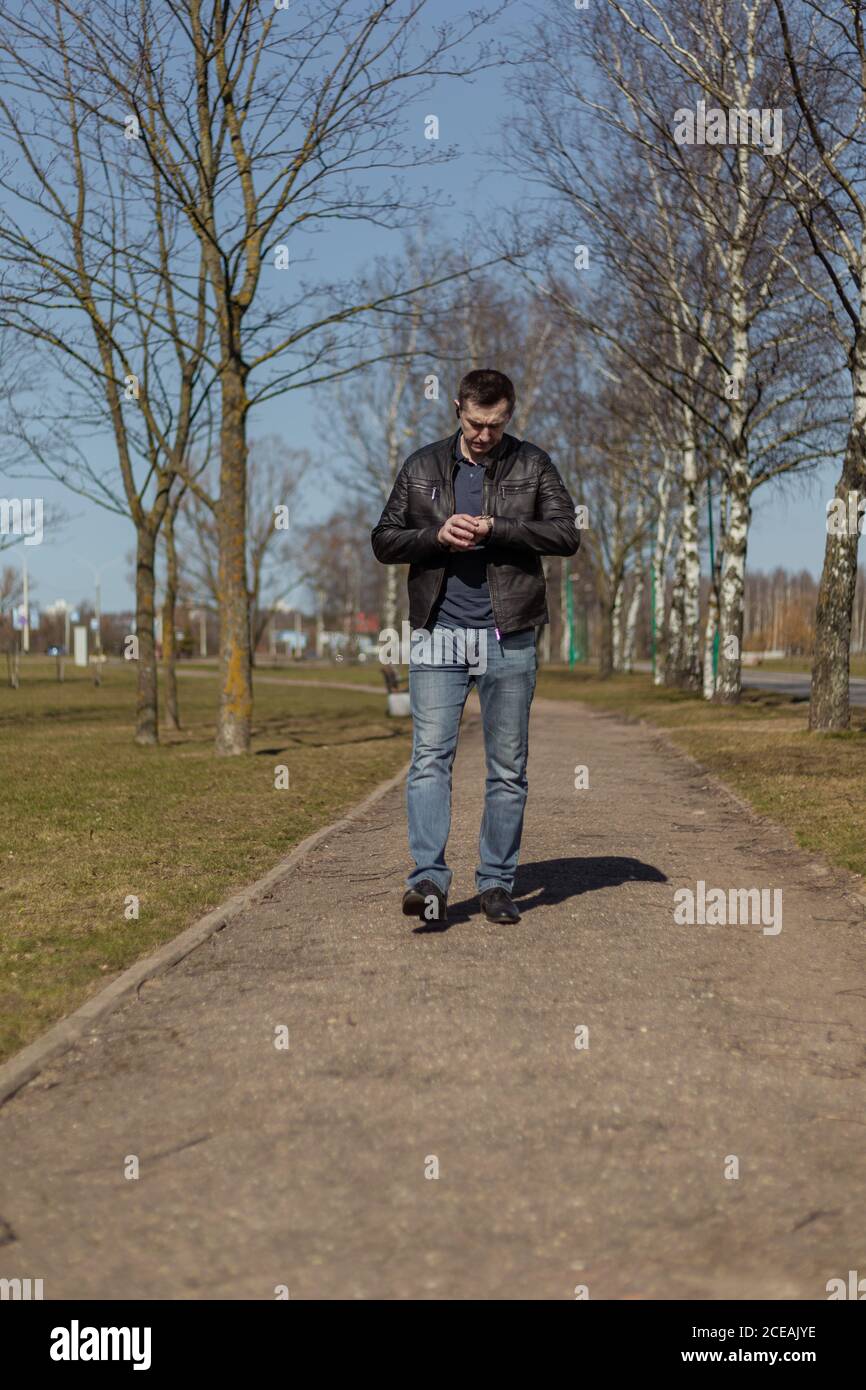 Joven adulto en una chaqueta de cuero negro y jeans paseos por el camino en un día soleado Foto de stock