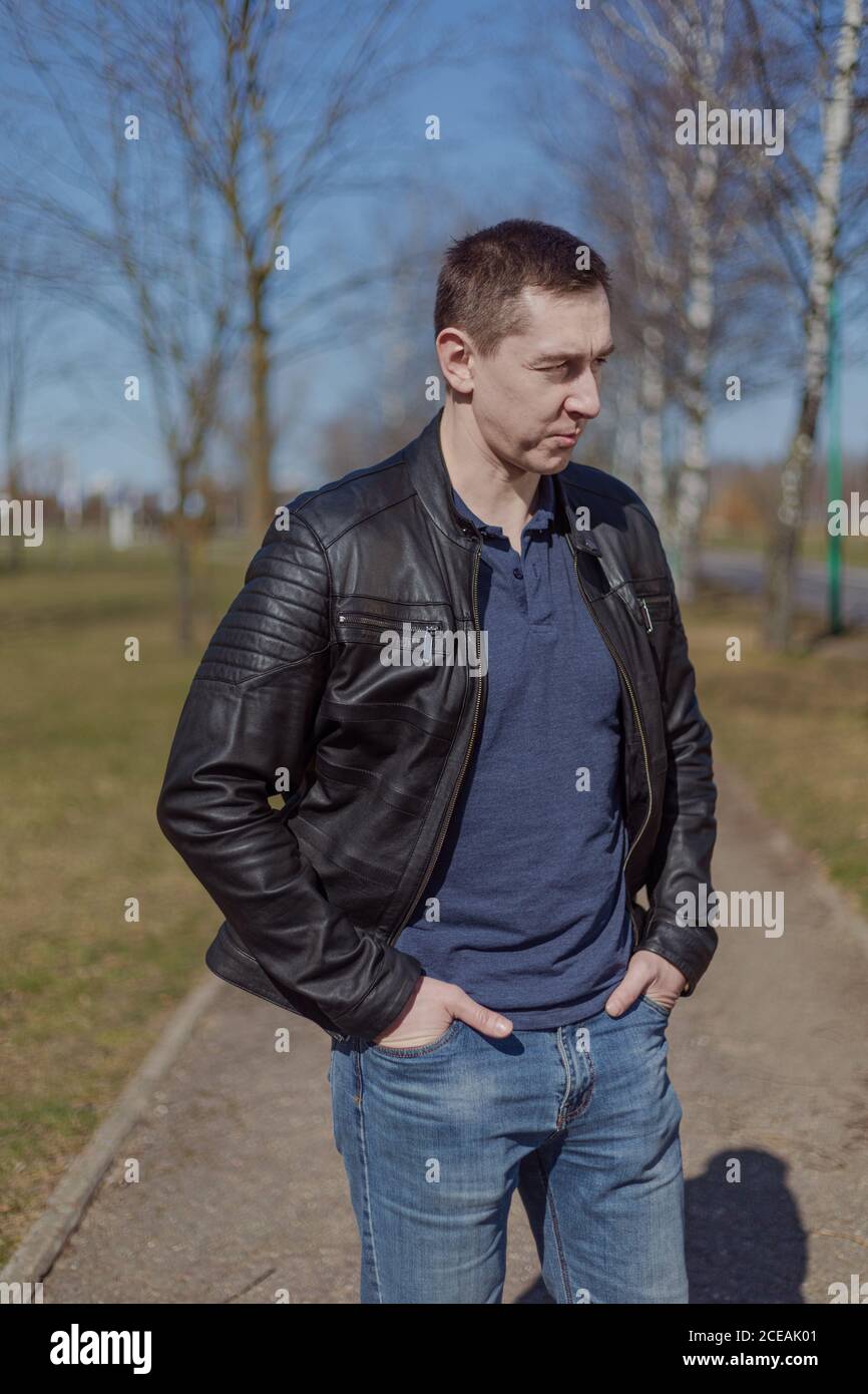 Joven adulto en una chaqueta de cuero negro y jeans paseos por el camino en un día soleado Foto de stock