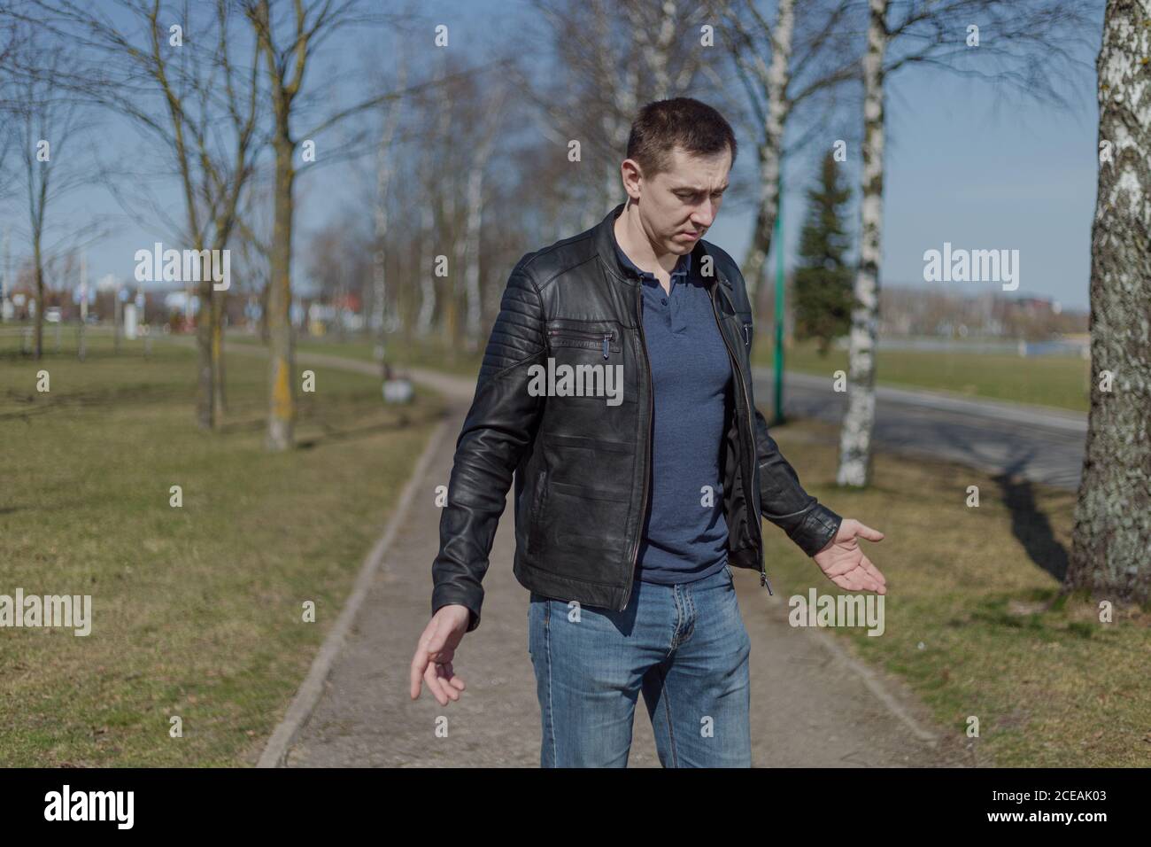 Joven adulto en una chaqueta de cuero negro y jeans paseos por el camino en un día soleado Foto de stock