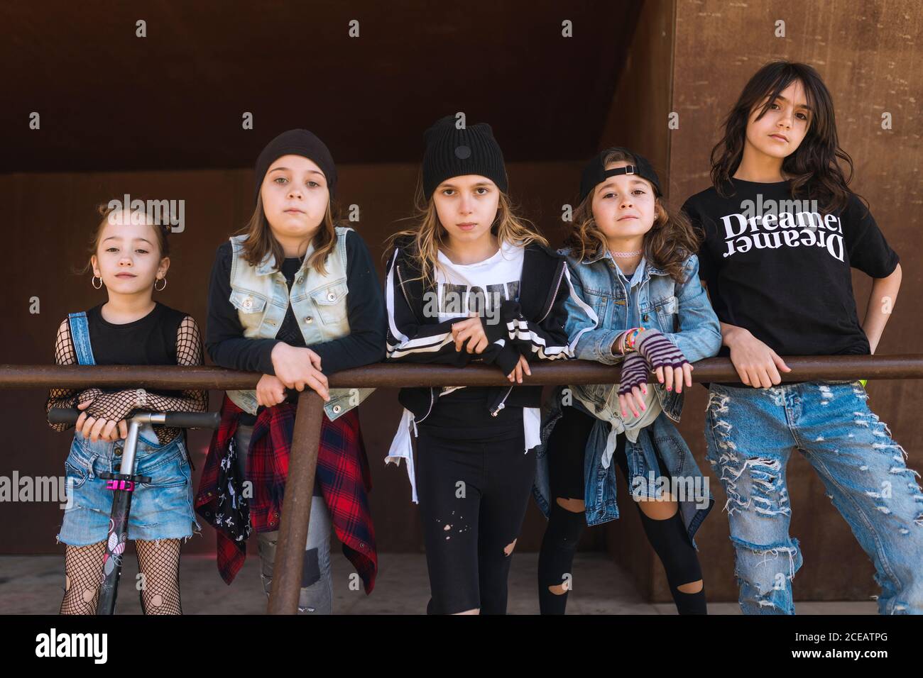 Chicas de moda y seguras con ropa rebelde de pie en fila frente a la valla  de metal mirando la cámara Fotografía de stock - Alamy