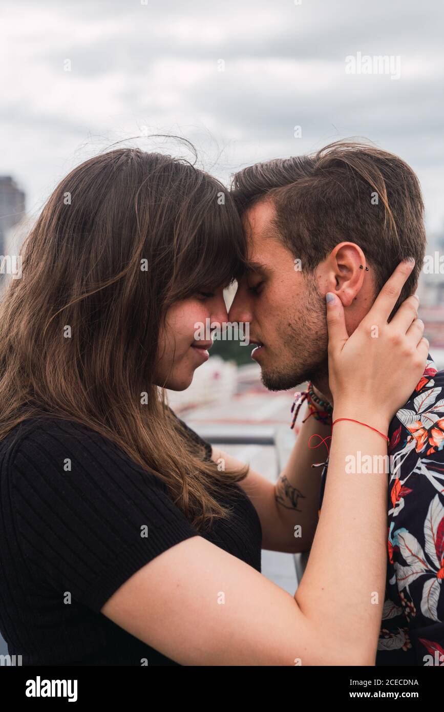 Pareja joven besando en un balcón y disfrutando de las vistas de una ciudad moderna Foto de stock