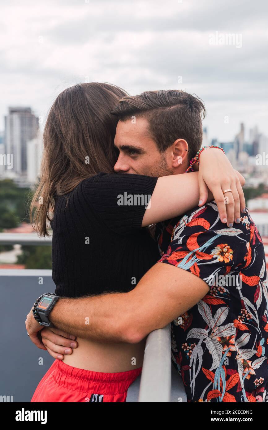 Una joven pareja abrazando un balcón y disfrutando de las vistas de una ciudad moderna Foto de stock