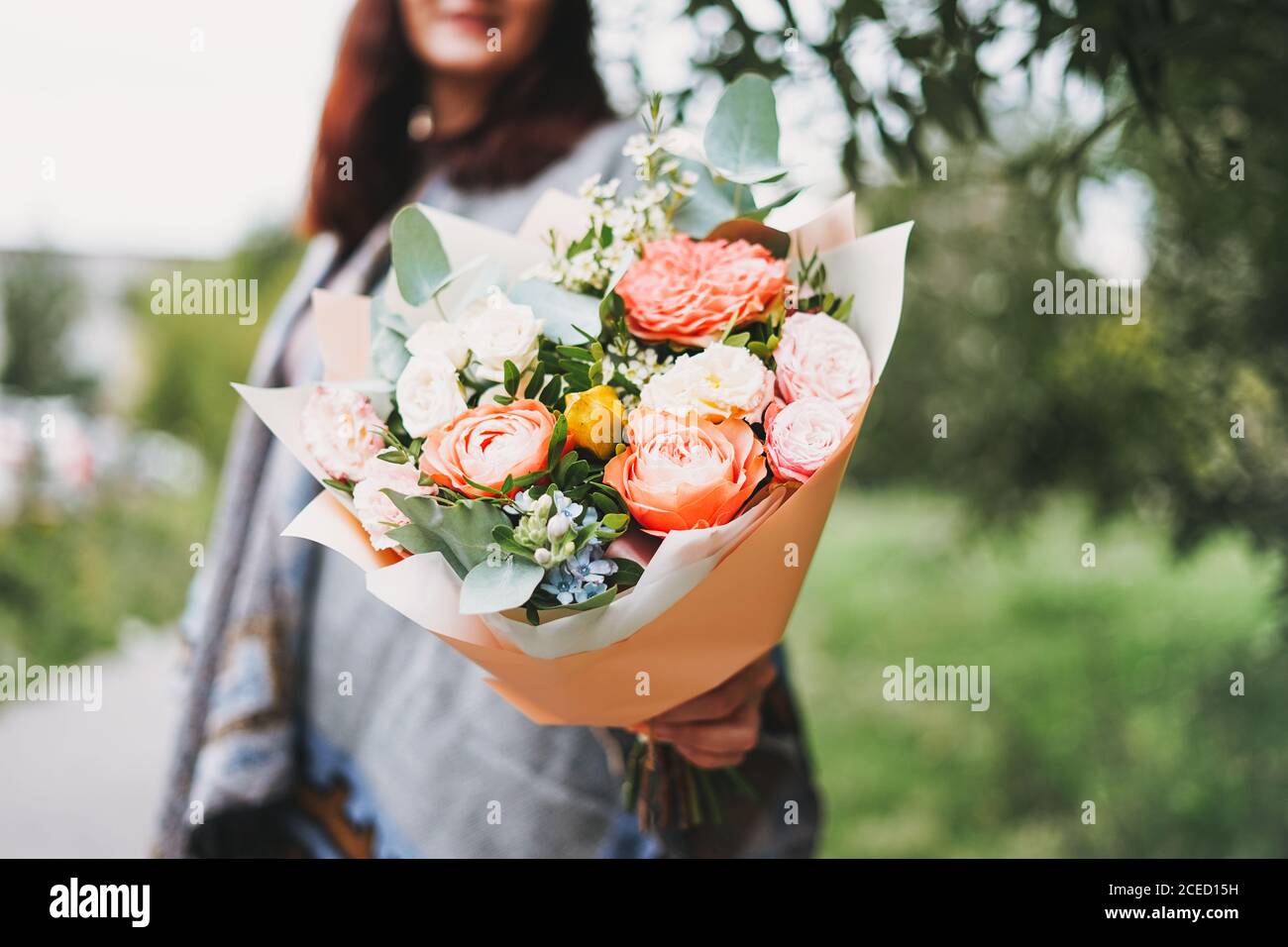 Joven mujer morena en poncho y jeans tiene un hermoso ramo de diferentes flores Foto de stock