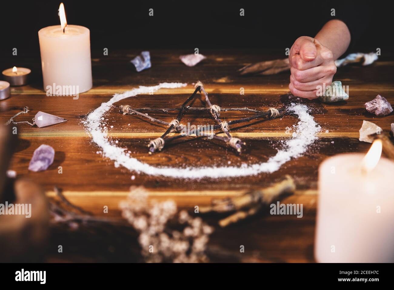 Mujer esparciendo sal sobre un pentagrama, ritual y ocultismo, ingredientes de brujería sobre mesa de madera Foto de stock