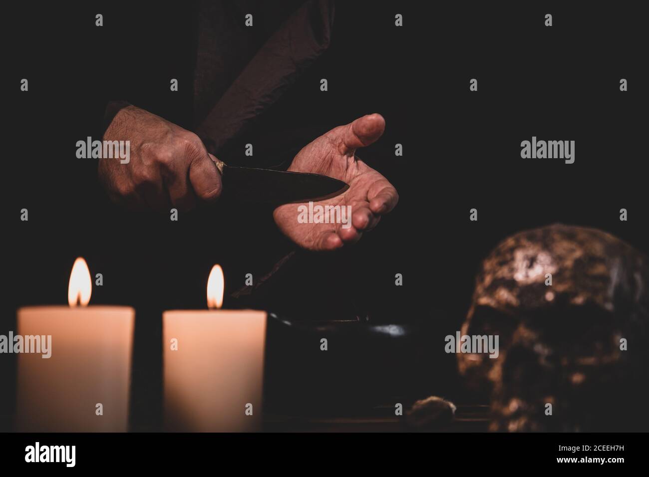 Ritual de sangre, preparación con un cuchillo, brujería o culto occultamente, fondo oscuro con velas y un cráneo humano Foto de stock