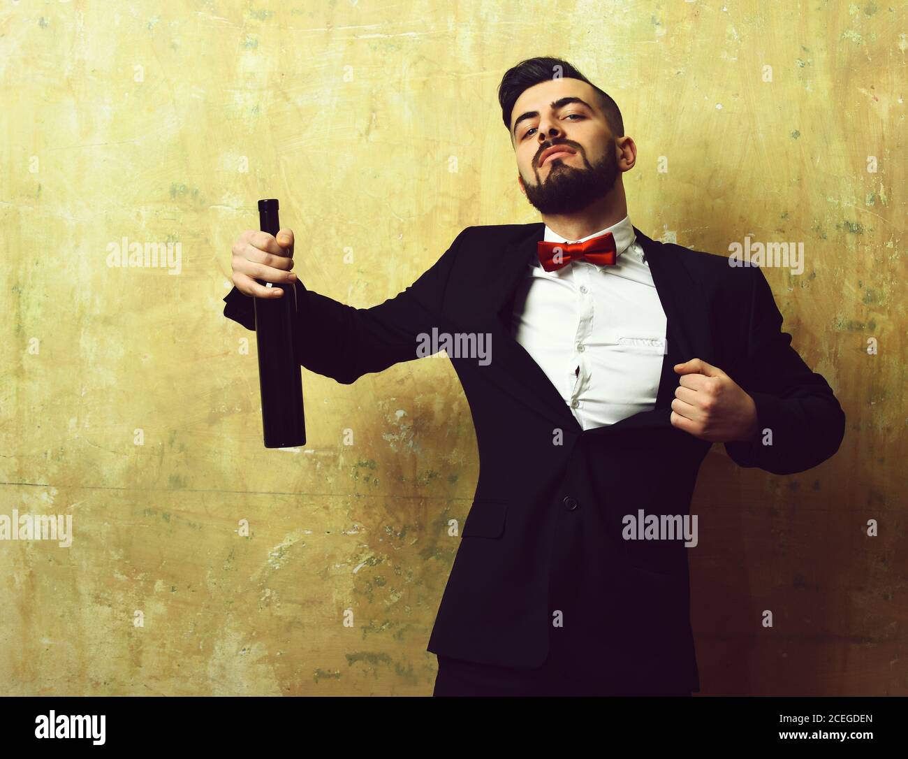 Concepto de fiesta del viernes por la noche y bebidas alcohólicas: Hombre  familiar sin afeitarse con botella de vino en traje negro y arco rojo sobre  fondo beige Fotografía de stock -