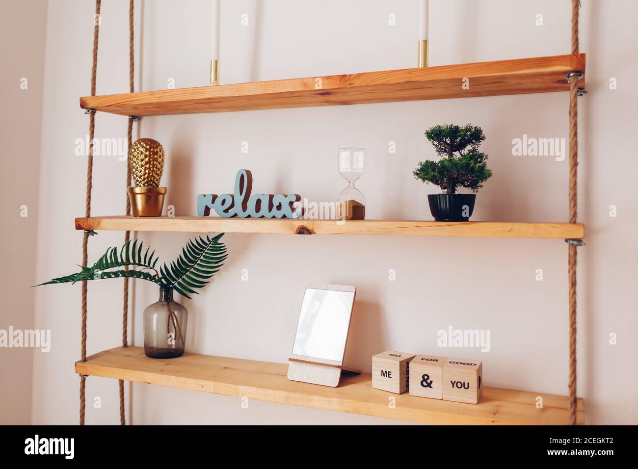 Estantería moderna de madera con piezas de decoración velas, espejo,  plantas colgando sobre cuerdas en pared blanca. Interior del hogar  Fotografía de stock - Alamy