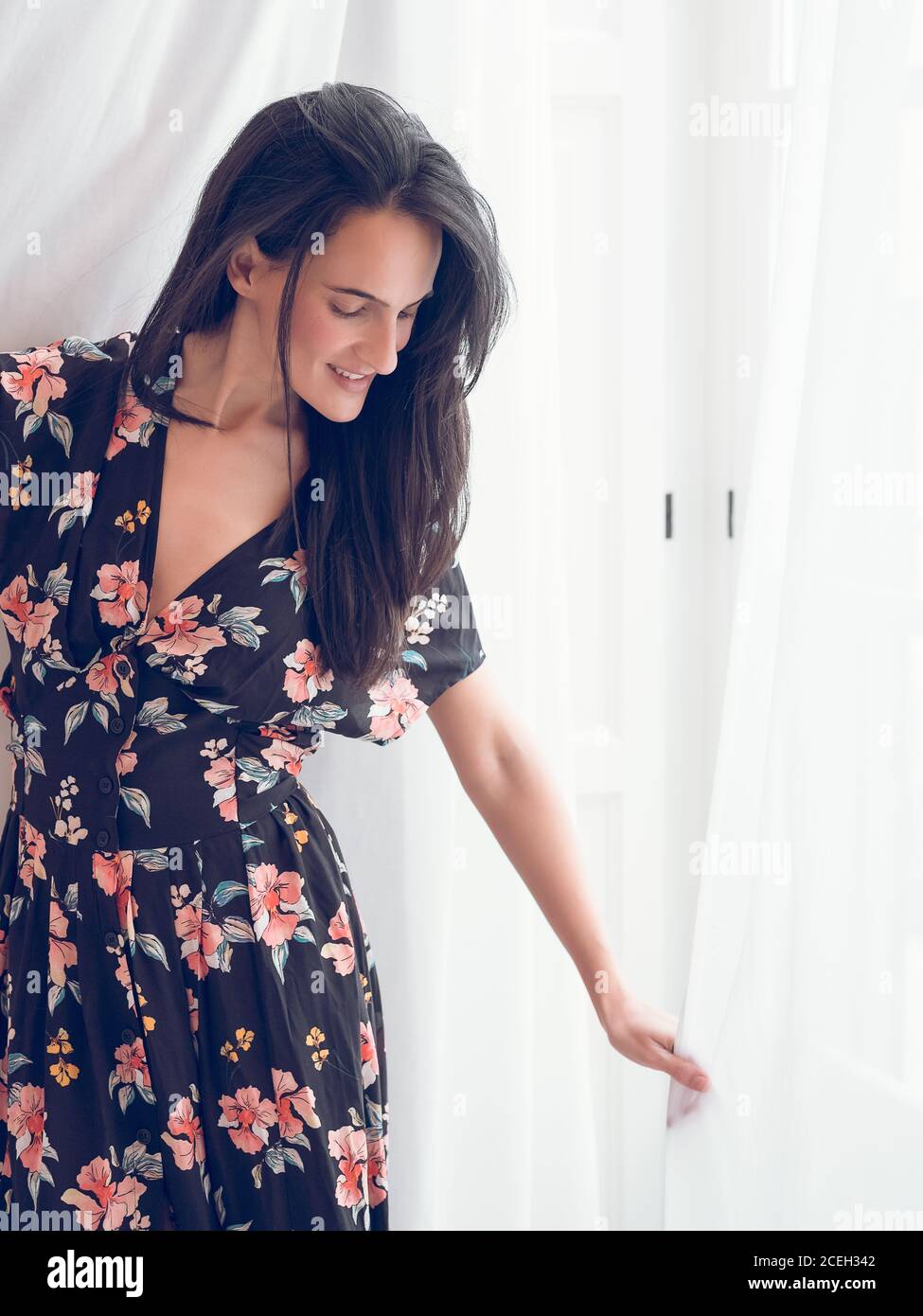 Hermosa mujer sonriente en vestido floral negro de pie sobre telón de fondo  blanco y mirando hacia abajo Fotografía de stock - Alamy