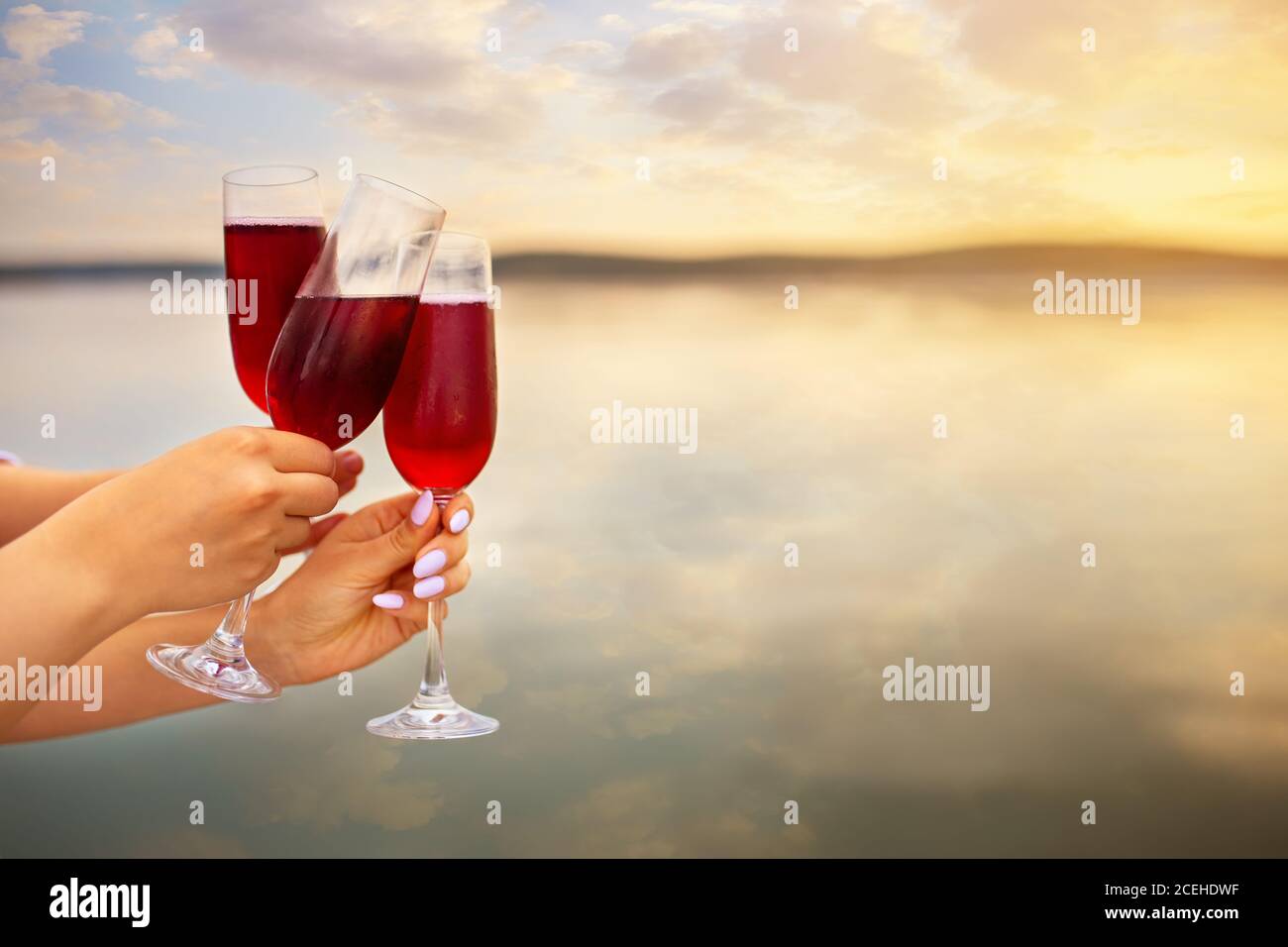 manos femeninas con copas de champán rojo haciendo pan tostado Foto de stock