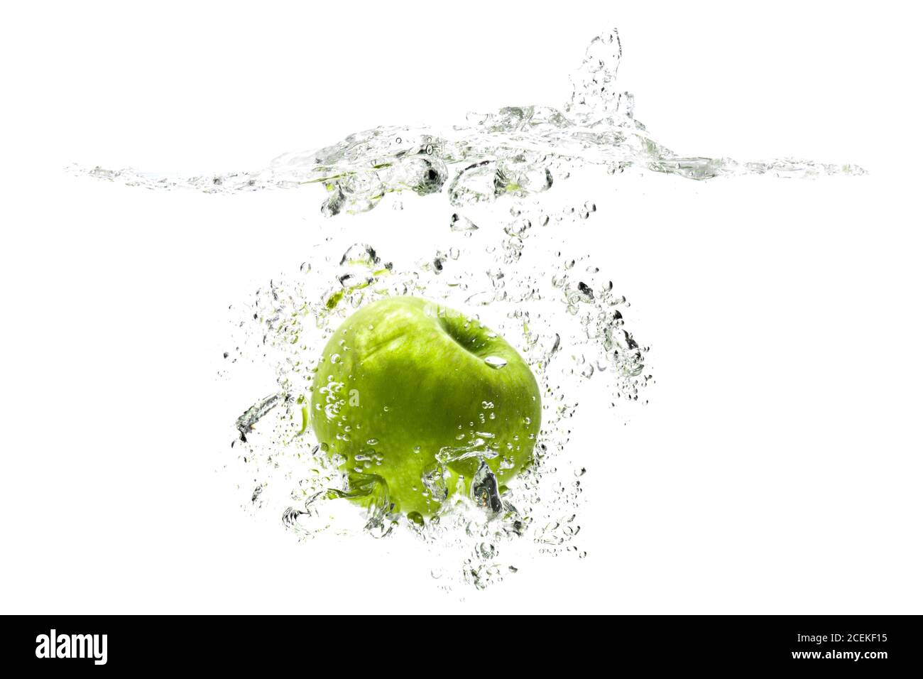 una manzana verde cayendo en el agua sobre un fondo blanco con salpicaduras, gotas y burbujas. Foto de stock