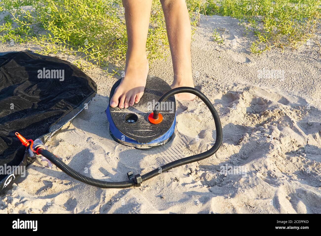 Una mujer con bomba de aire para pies bombea un colchón inflable o una cama  de aire en la playa de arena. El pie infla el colchón de aire con la bomba