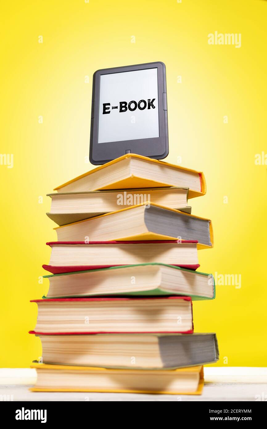 Lectura y conocimiento. E-libro encima de una pila de libros sobre un fondo  amarillo. Vertical. Concepto de educación y aparatos electrónicos  Fotografía de stock - Alamy