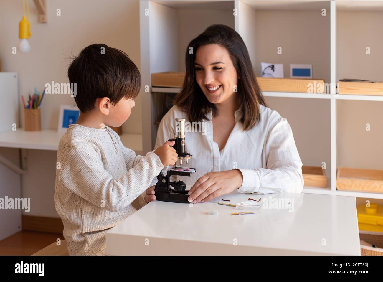 Lillte Kid explorando la ciencia con un microscopio y ayuda de madre o maestro. Resolución de problemas en casa. Comunidad de aprendizaje. Escuela Montessori Foto de stock