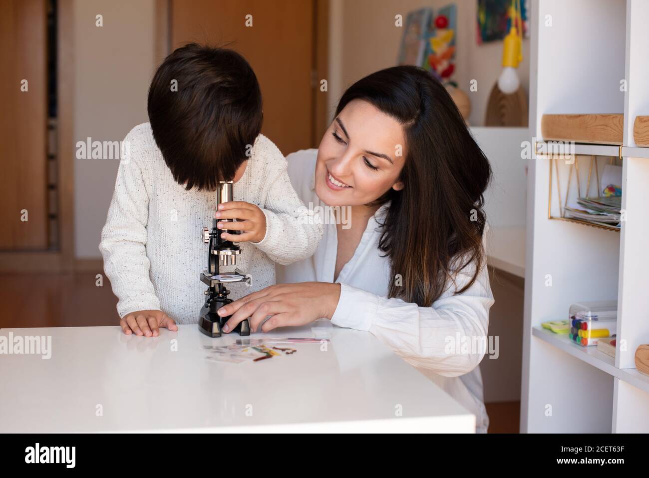 Lillte Kid explorando la ciencia con un microscopio y ayuda de madre o maestro. Resolución de problemas en casa. Comunidad de aprendizaje. Escuela Montessori Foto de stock