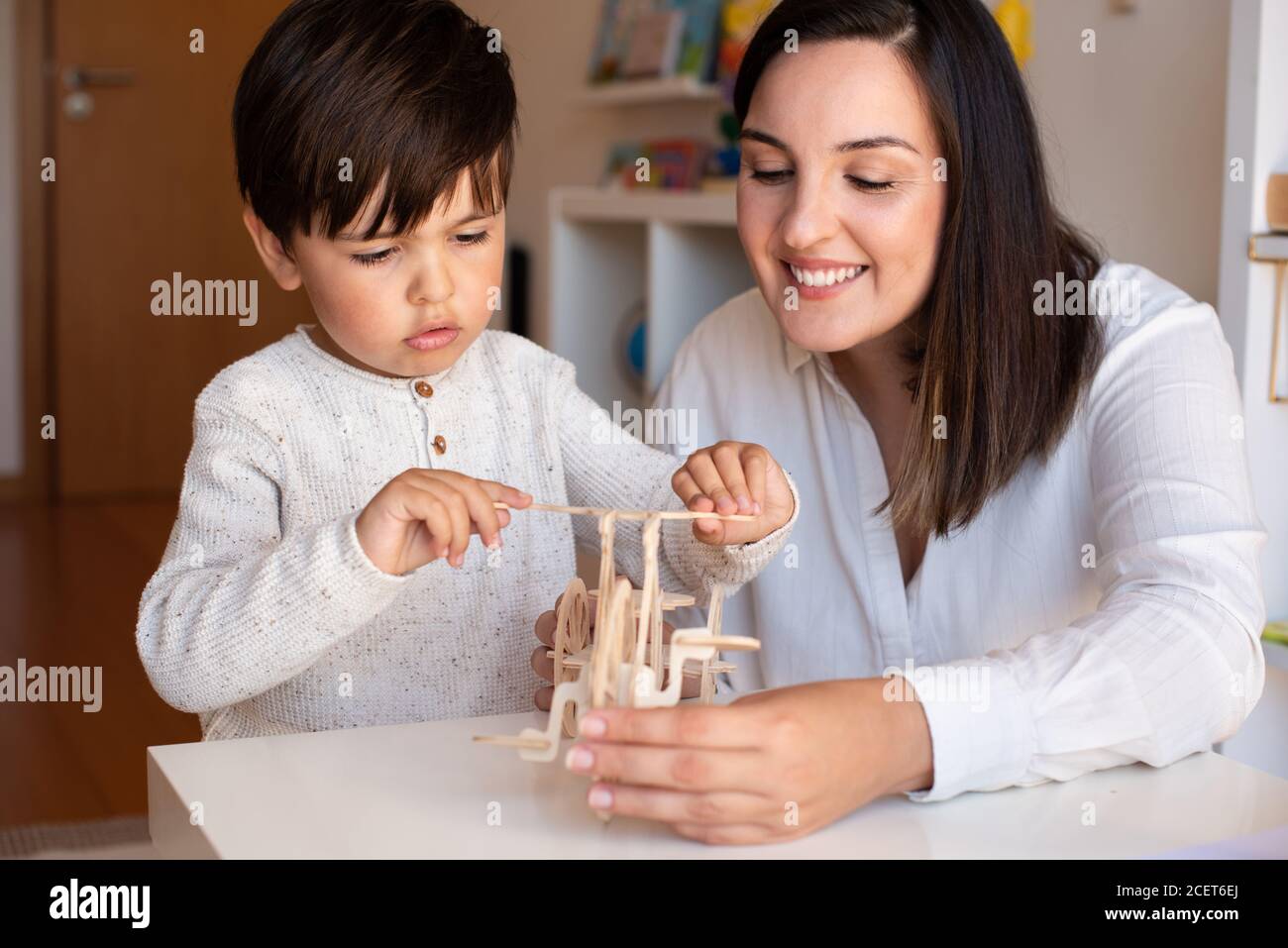 Liltle Preschooler Kid jugando con madera 3d rompecabezas y maestro educador ayuda. Resolución de problemas en casa. Comunidad de aprendizaje. Escuela Montessori Foto de stock