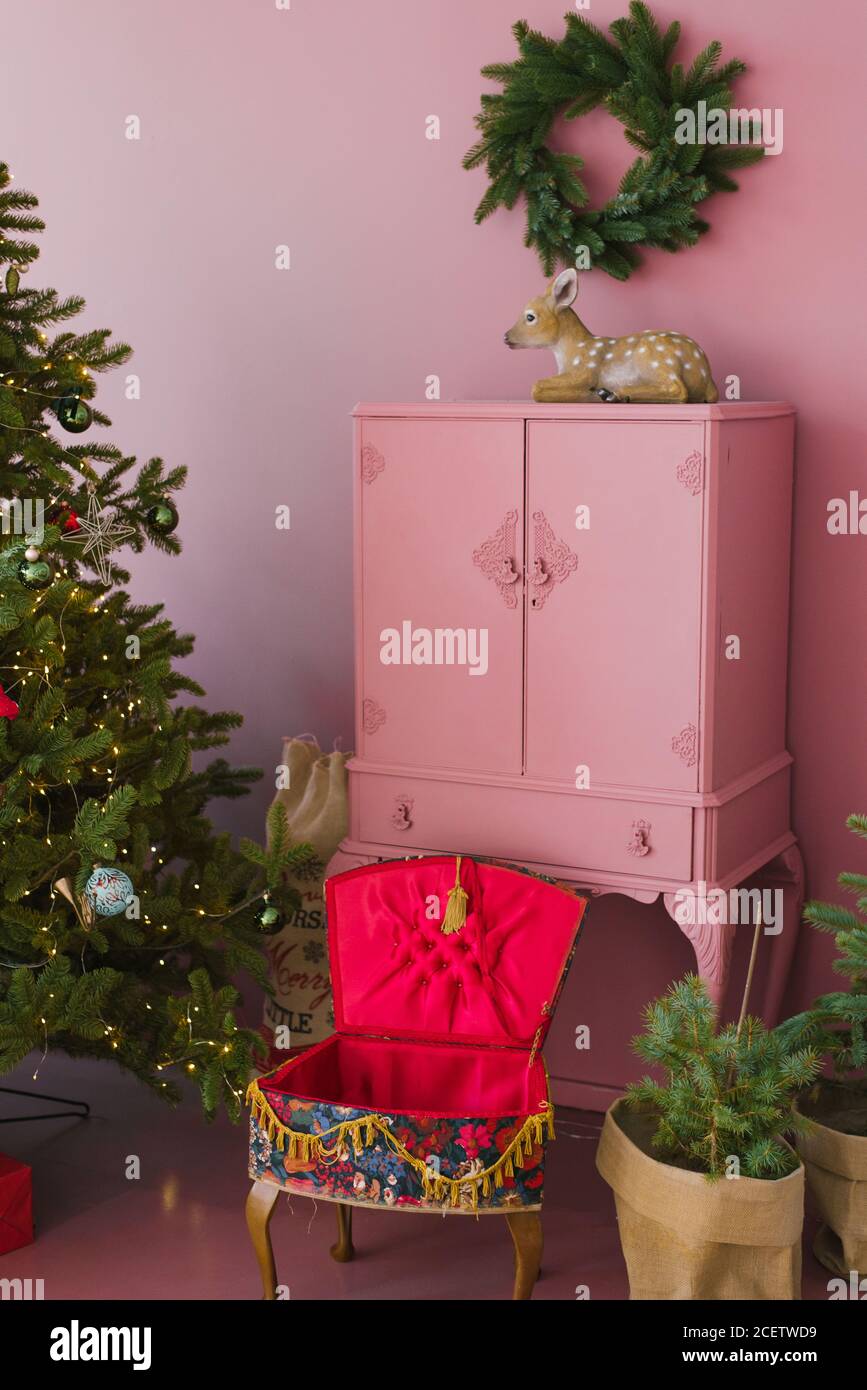 Caja de cajones de época rosa, árbol de Navidad y corona sobre el pecho de cajones, statuette de ciervo en la sala de estar de la casa Foto de stock