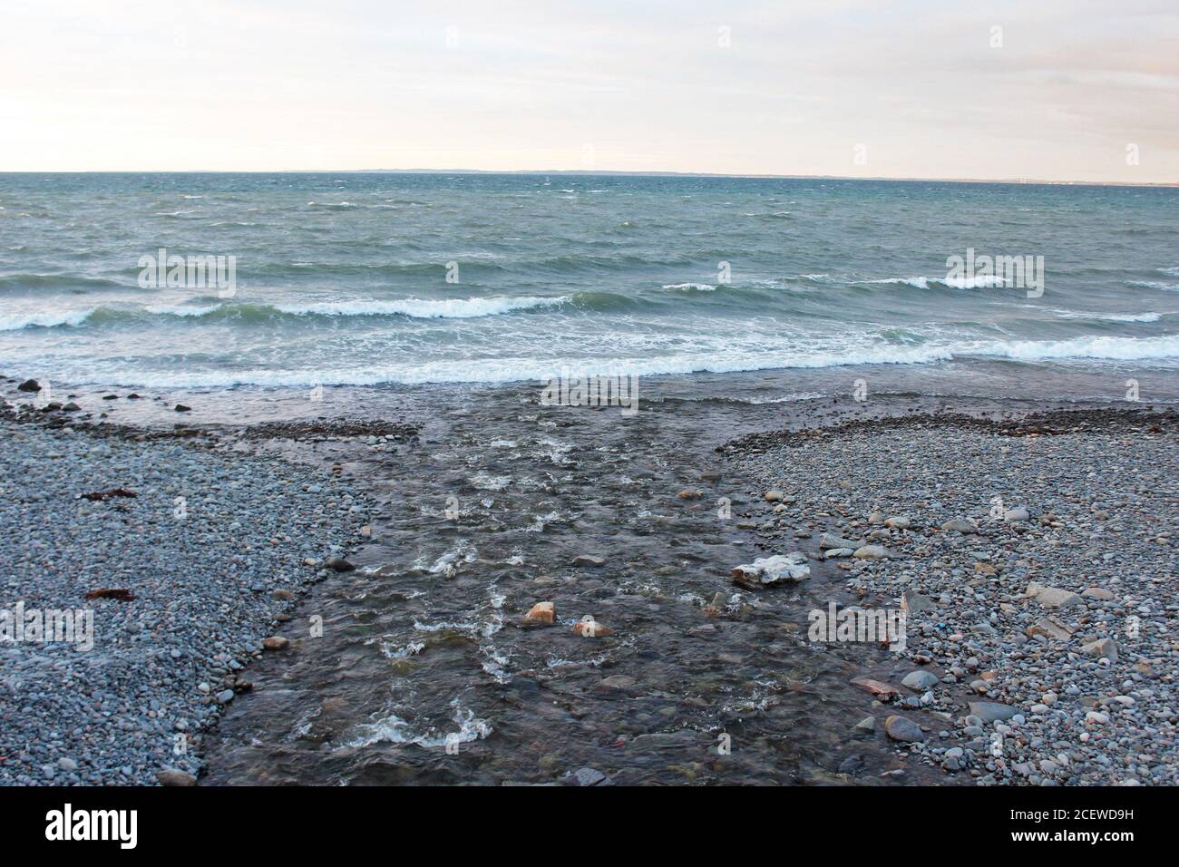 Punto donde un arroyo se encuentra con el mar entrecortado en una playa rocosa en Trefor, Gales del Norte Foto de stock