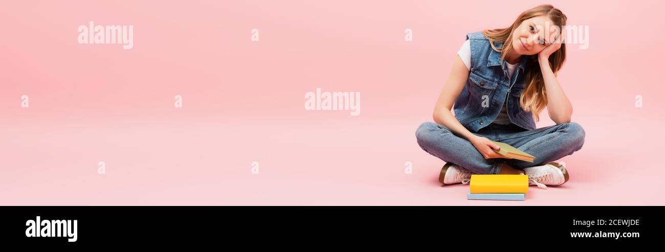 foto panorámica de una joven con ropa vaquera sentada suelo cerca de los  libros y la cabeza con la mano encima rosa Fotografía de stock - Alamy