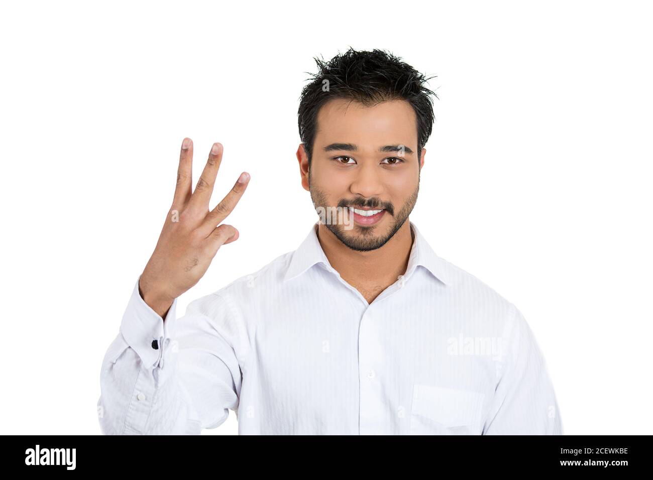 Primer retrato de un joven guapo dando un gesto de tres dedos con la mano aislada sobre fondo blanco. Expresión facial de emoción positiva Foto de stock