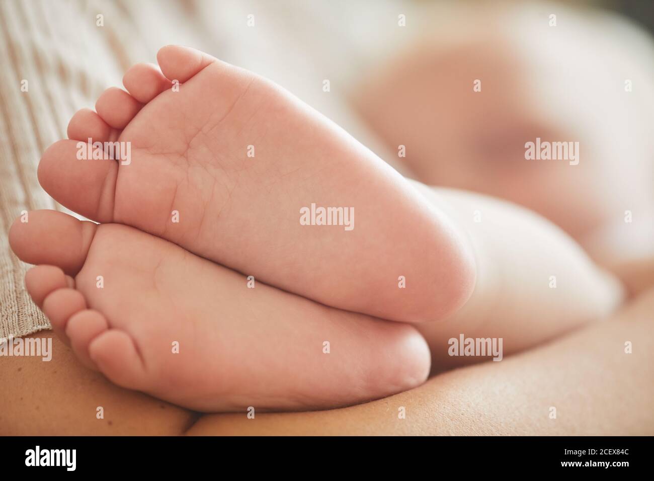 Tiro de cerca horizontal de los encantadores pies del bebé caucásico, su madre lo está abrazando Foto de stock
