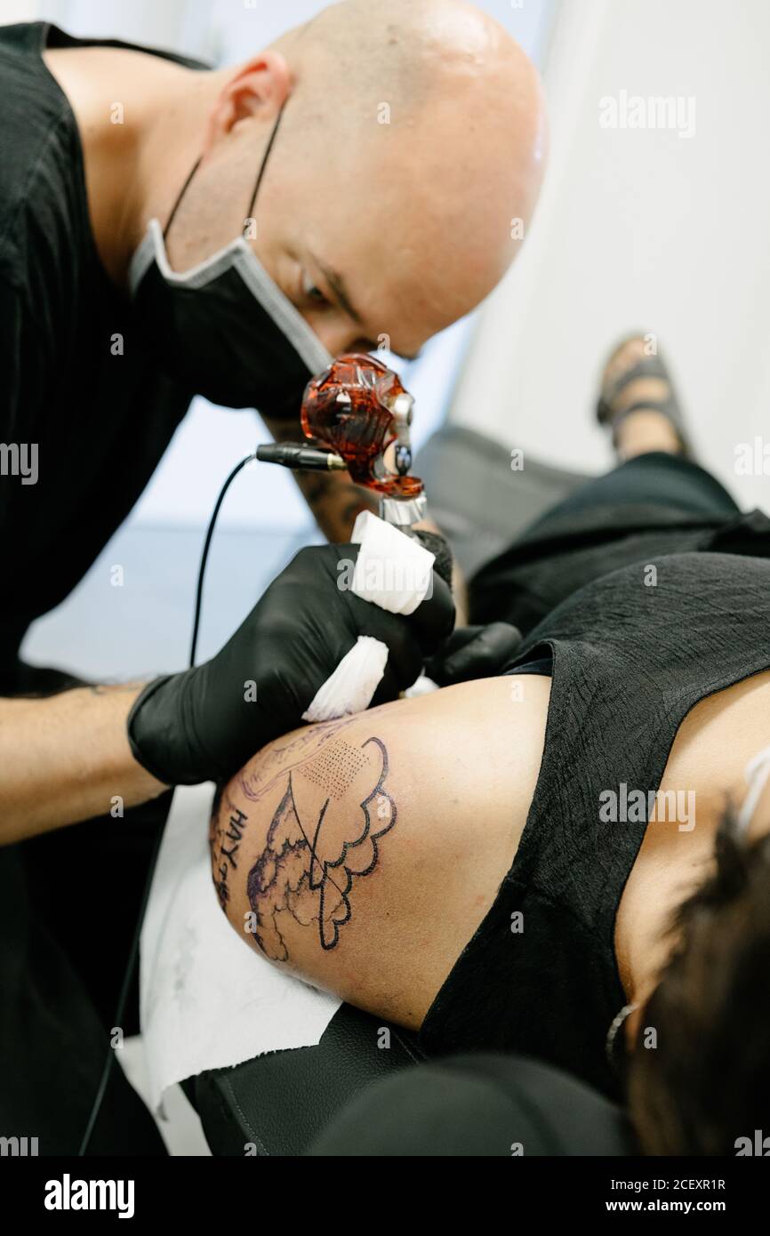 Recortar tatuaje masculino con máquina de hacer tatuaje en el brazo de la  mujer acostada sobre la mesa en el salón Fotografía de stock - Alamy