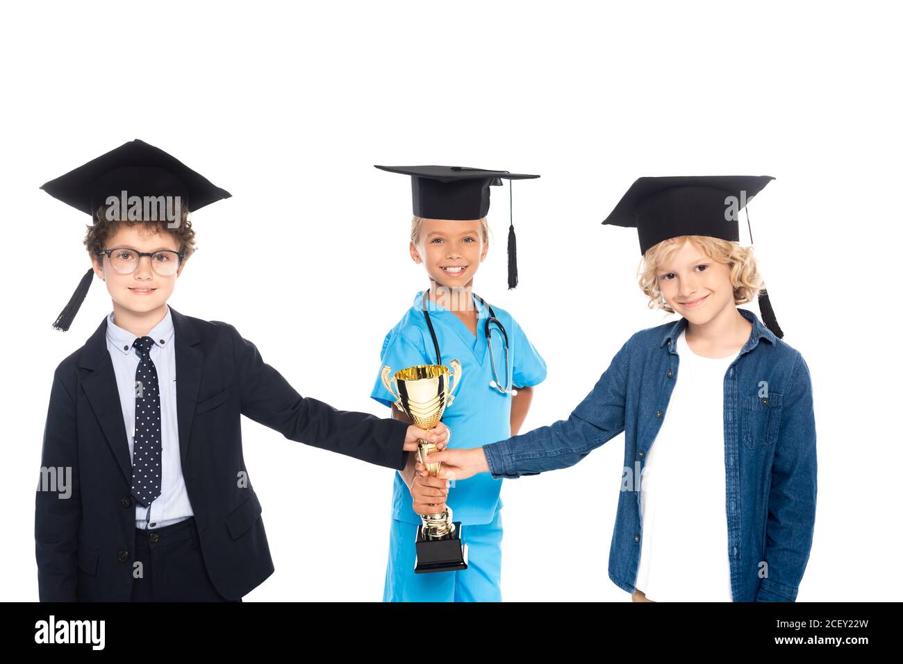 niños en gorras de graduación vestidos con trajes de diferentes profesiones sosteniendo trofeo dorado aislado sobre blanco Foto de stock