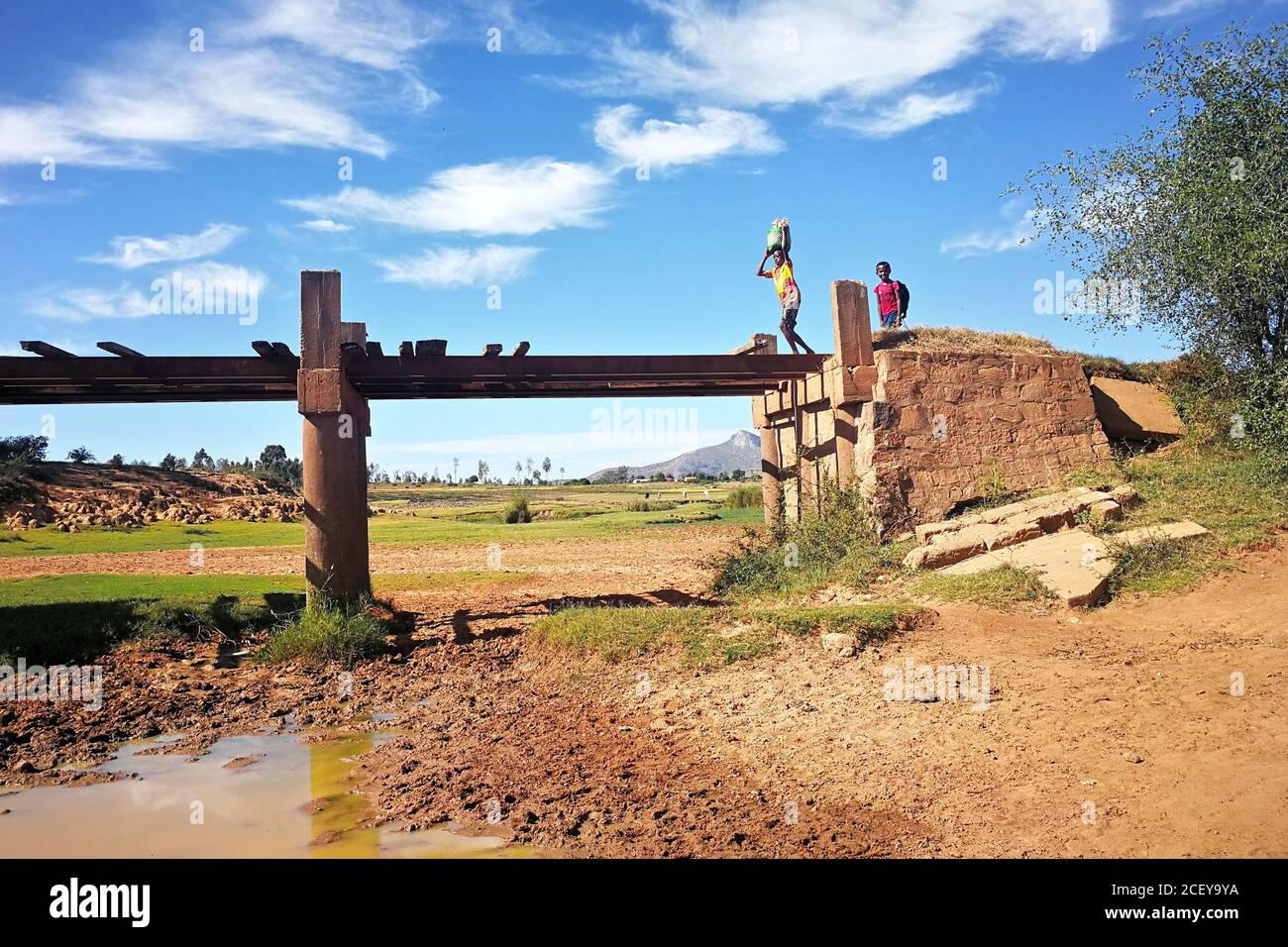 Ambalavao, Madagascar - 27 de abril de 2019: Desconocido Malagasy niño llevando la bolsa en su cabeza sobre un simple puente, otro sonriendo detrás de él, típico Mada Foto de stock