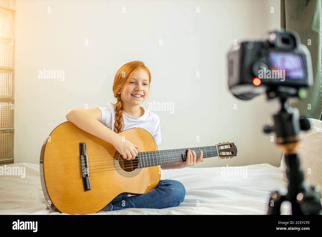 retrato de la hermosa niña caucásica blogger tocando la guitarra en la cámara. adorable chica sentada mostrando, realizando nueva melodía para los suscriptores. vl Foto de stock