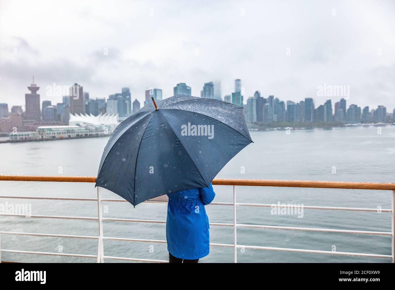 Mujer de crucero de lujo que sale del puerto observando el horizonte de la ciudad de Vancouver bajo la lluvia con paraguas. Destino del viaje del barco en otoño. Foto de stock