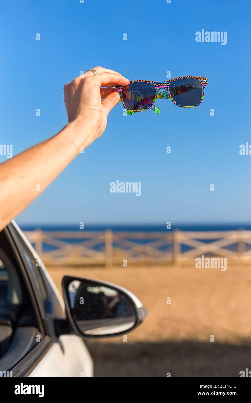 Brazo en la ventana del coche mostrando cegadores de sol en la orilla con el mar Foto de stock