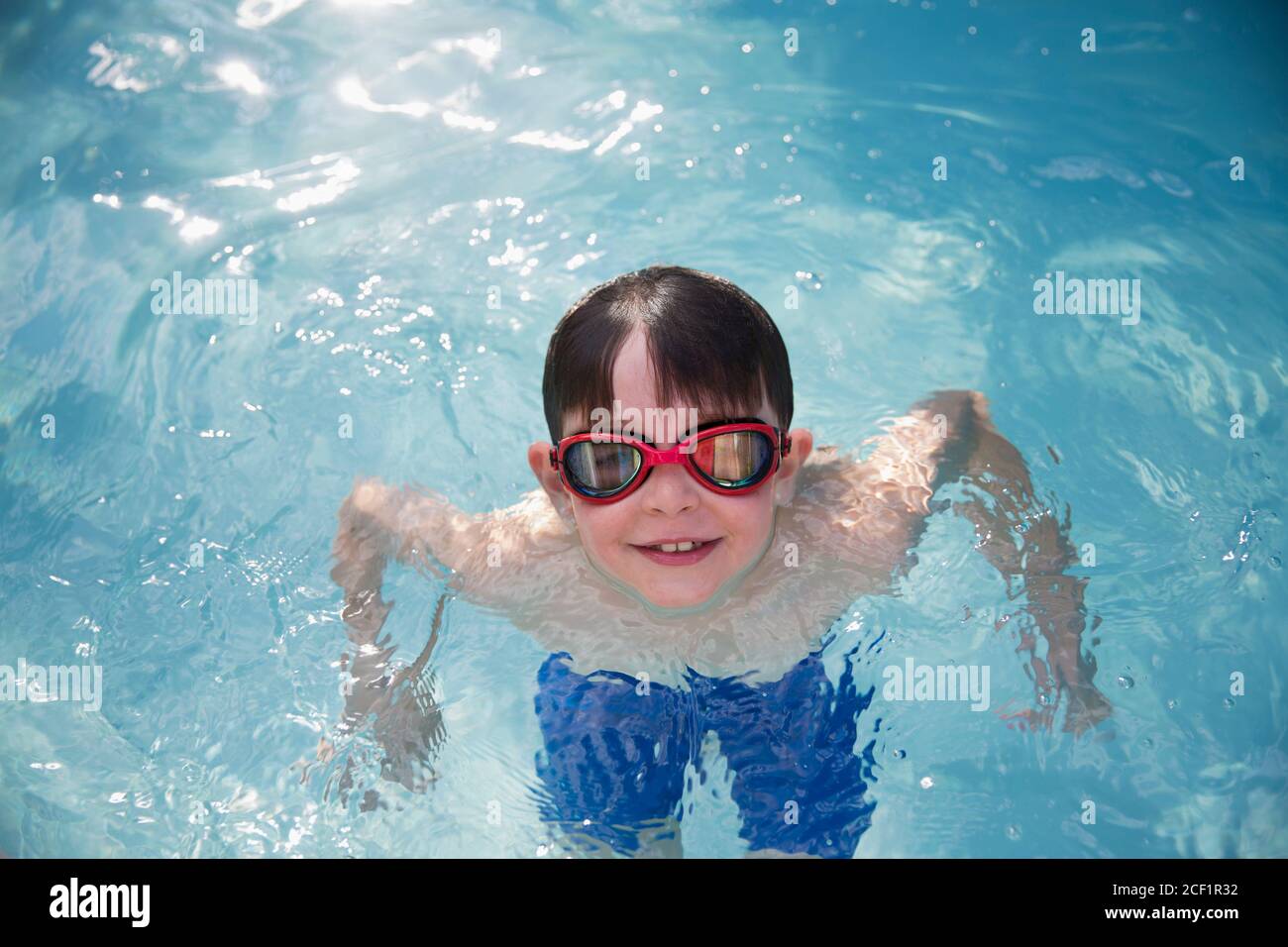 Retrato sonriente niño en gafas de natación en la piscina soleada Foto de stock