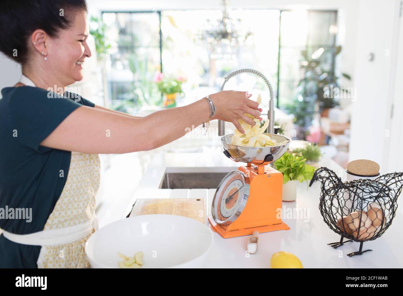 Mujer sonriente pesando manzanas rebanadas para hornear en la cocina Foto de stock