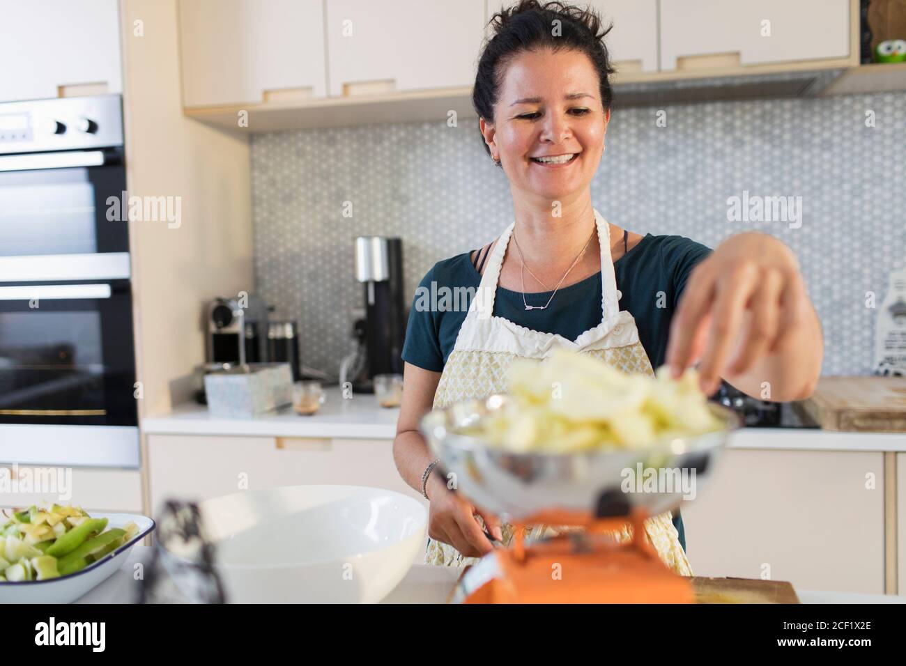 Mujer sonriente pesando manzanas para hornear en la cocina Foto de stock