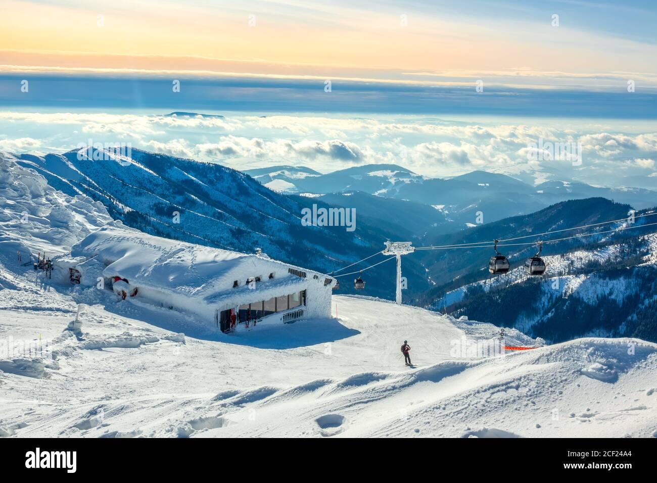 Montañas de invierno. Picos nevados y niebla en los valles. Cielo azul y rosa sobre la pista de esquí. Telesilla y bar. Foto de stock