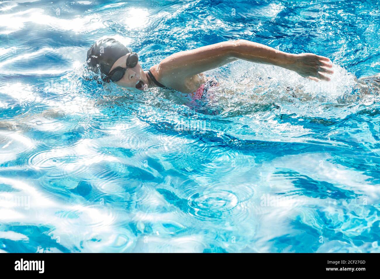 Mujer con gorro de baño y gafas nadando en una piscina. Foto de stock