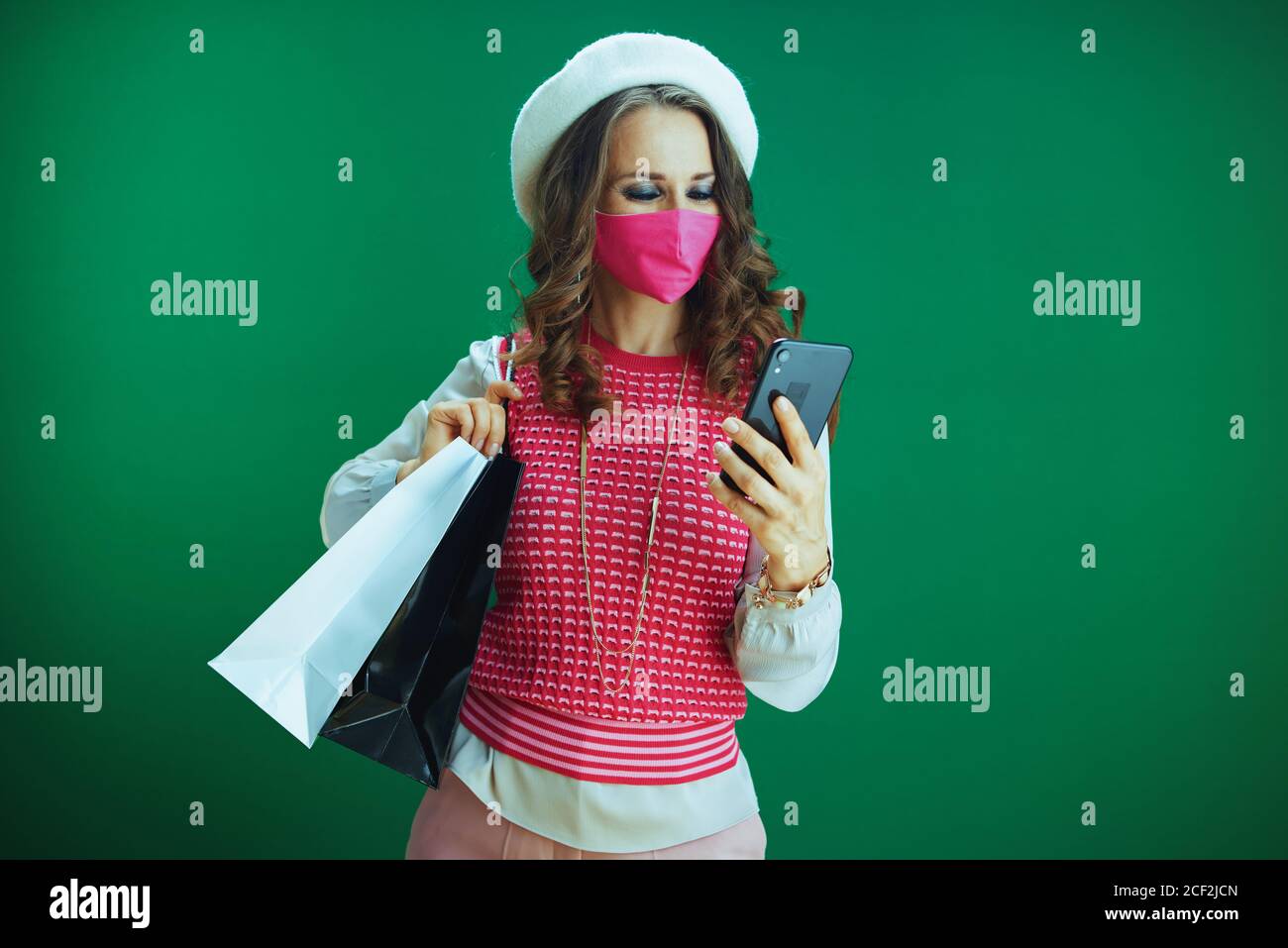 La vida durante la pandemia del covid-19.elegante comprador femenino en camisa sin mangas rosa con máscara médica rosa y bolsas de compras comprando en Internet en un smarpp Foto de stock